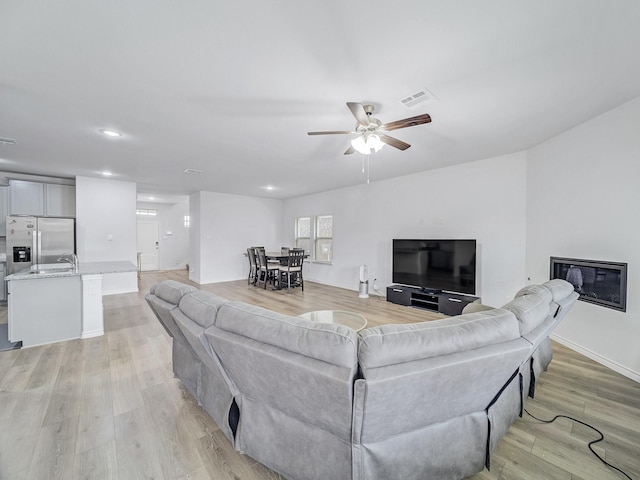 living area with recessed lighting, visible vents, light wood-style floors, a glass covered fireplace, and ceiling fan