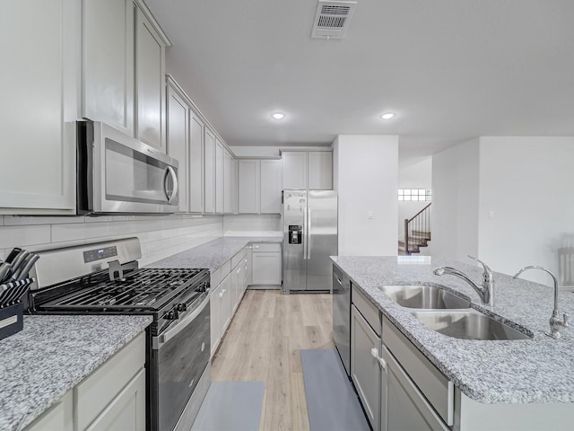 kitchen with visible vents, a kitchen island with sink, stainless steel appliances, light wood-type flooring, and a sink