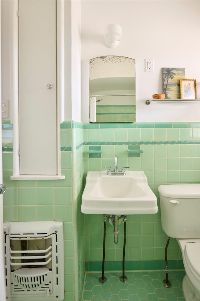 bathroom featuring wainscoting, toilet, heating unit, a sink, and tile walls