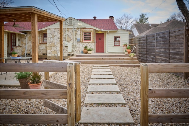 view of front of property featuring a patio, fence, stone siding, roof with shingles, and a chimney