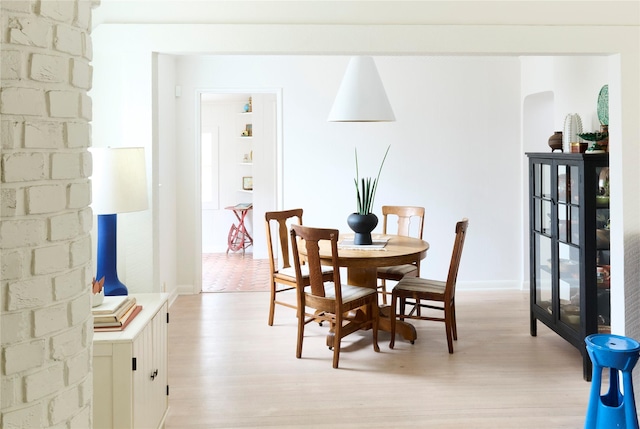 dining room featuring arched walkways, light wood finished floors, and baseboards