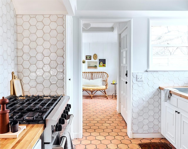 kitchen with tile walls, light tile patterned floors, wooden counters, white cabinets, and stainless steel range with gas stovetop