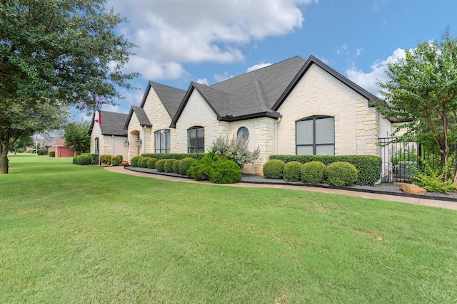 french country home with brick siding, a shingled roof, stone siding, and a front yard