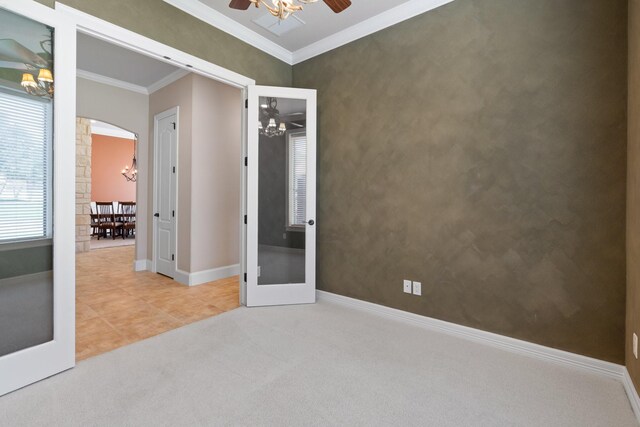 carpeted empty room with a ceiling fan, crown molding, a chandelier, baseboards, and arched walkways