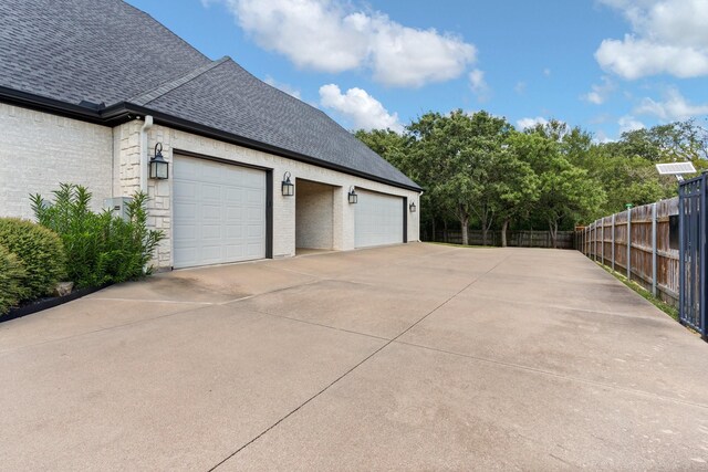 view of property exterior with fence, a shingled roof, driveway, brick siding, and a garage