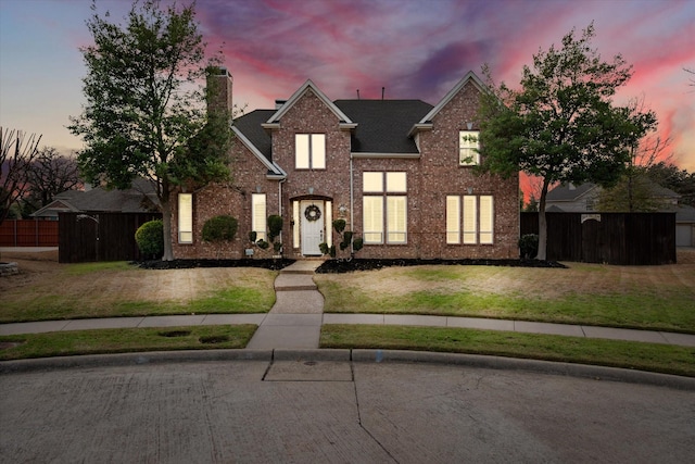 traditional home featuring a shingled roof, a chimney, fence, a front lawn, and brick siding