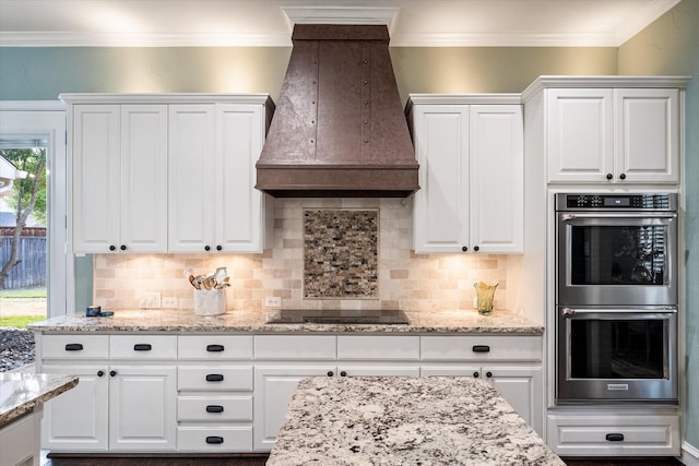 kitchen with crown molding, black electric stovetop, double oven, white cabinetry, and premium range hood