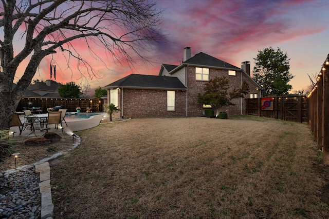 back of house featuring a fenced backyard, brick siding, a lawn, a fenced in pool, and a patio area