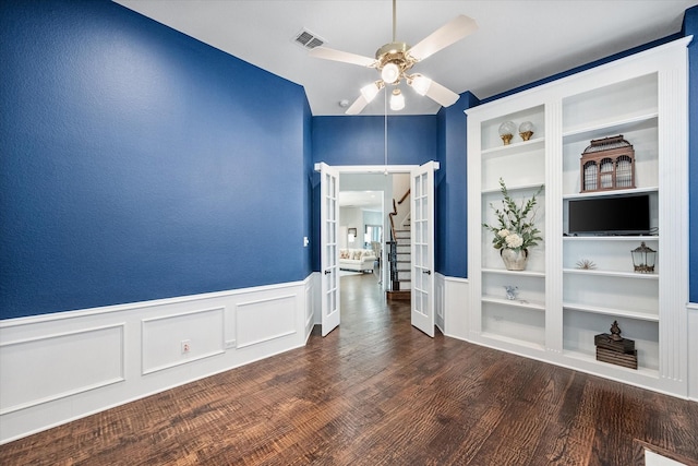 spare room featuring built in shelves, wood finished floors, visible vents, a ceiling fan, and wainscoting