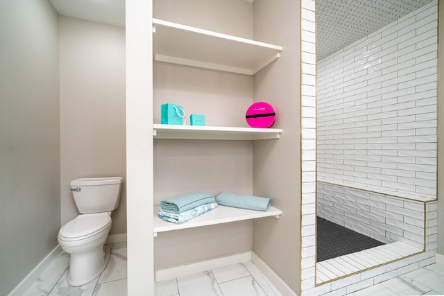 bathroom featuring marble finish floor, baseboards, a tile shower, and toilet