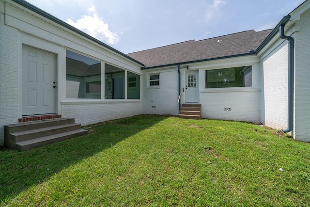 rear view of house with brick siding, roof with shingles, a lawn, entry steps, and crawl space