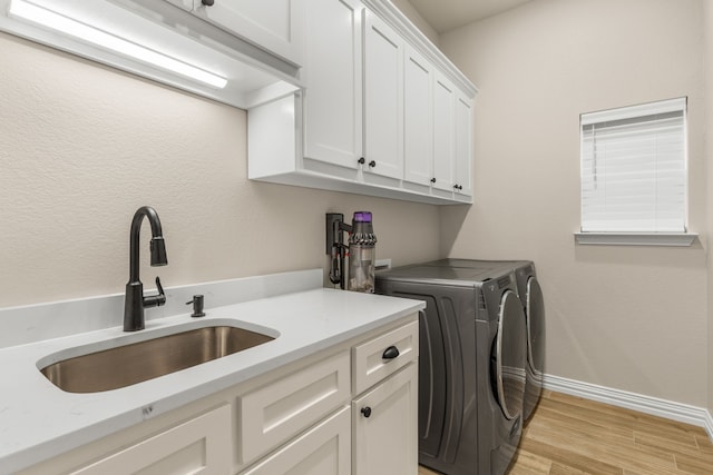 laundry room with light wood-type flooring, washer and dryer, cabinet space, and a sink