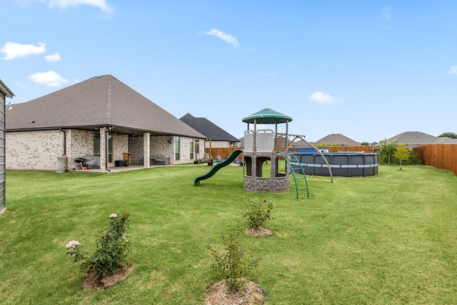 view of playground featuring a lawn, a patio area, a fenced backyard, and a fenced in pool