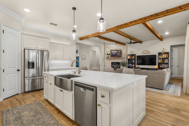 kitchen featuring visible vents, light wood-style flooring, stainless steel appliances, a stone fireplace, and a sink