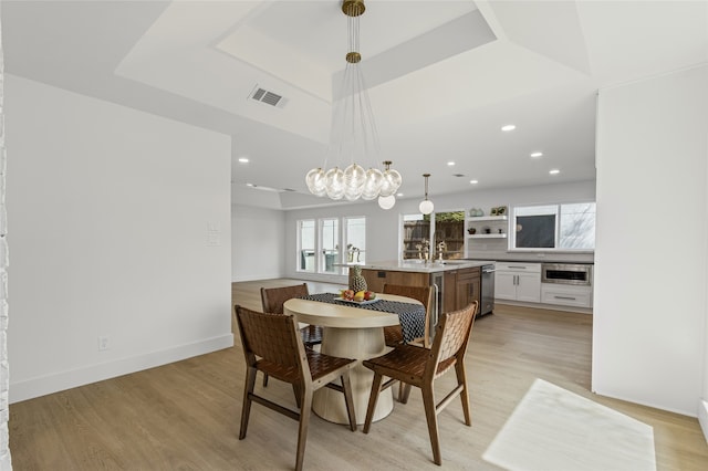 dining room with light wood-type flooring, a raised ceiling, visible vents, and baseboards