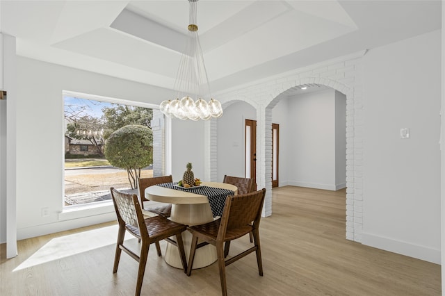 dining area with light wood-style floors, a tray ceiling, arched walkways, and baseboards