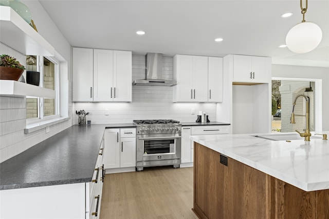 kitchen featuring a sink, wall chimney range hood, high end stove, and a wealth of natural light