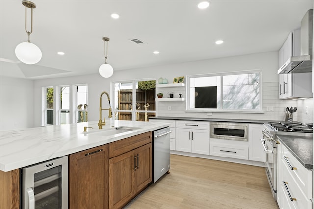 kitchen featuring wine cooler, stainless steel appliances, a sink, visible vents, and wall chimney range hood