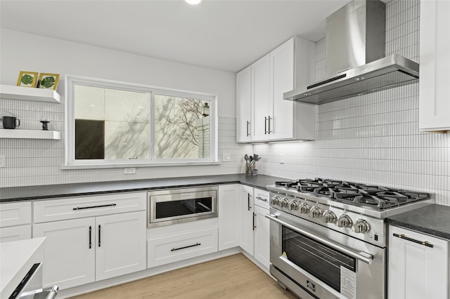 kitchen with wall chimney exhaust hood, appliances with stainless steel finishes, dark countertops, and white cabinetry