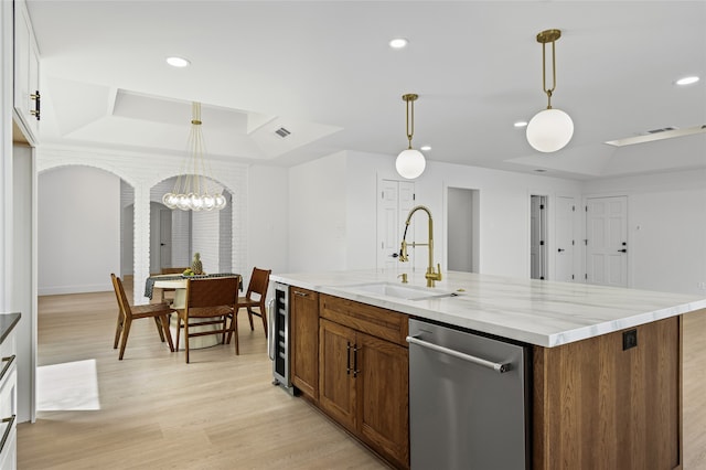 kitchen with a sink, dishwasher, light wood finished floors, a raised ceiling, and a center island with sink