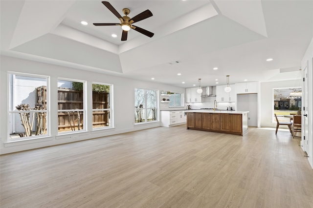 unfurnished living room featuring light wood finished floors, a raised ceiling, a ceiling fan, and recessed lighting