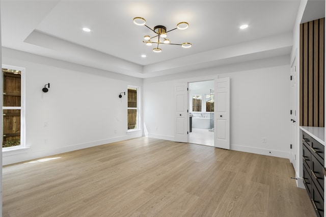 interior space featuring a chandelier, a tray ceiling, light wood-style flooring, and baseboards