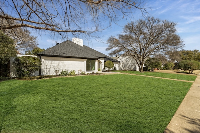 view of side of property with brick siding, a lawn, a chimney, and roof with shingles