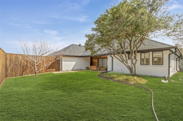 view of front facade featuring a fenced backyard, a front yard, roof with shingles, and brick siding