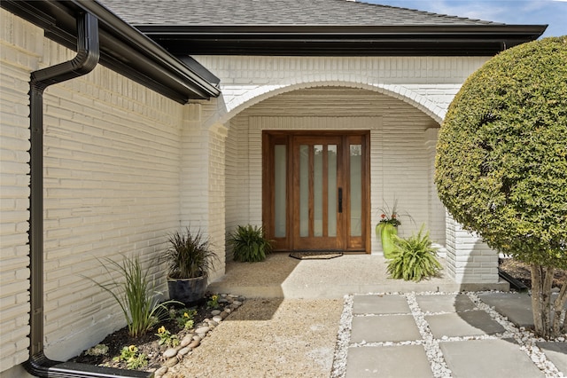 doorway to property featuring brick siding and roof with shingles