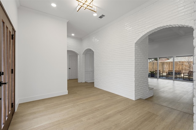 unfurnished room featuring light wood finished floors, brick wall, arched walkways, and crown molding