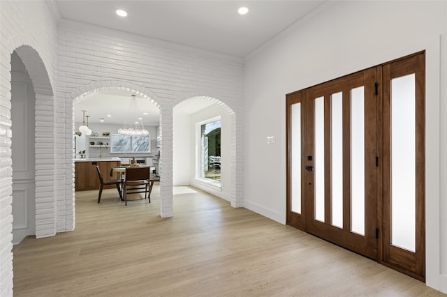 foyer with arched walkways, light wood-style flooring, recessed lighting, brick wall, and ornamental molding