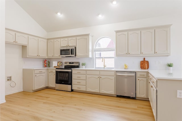 kitchen with lofted ceiling, light wood-style flooring, stainless steel appliances, and a sink