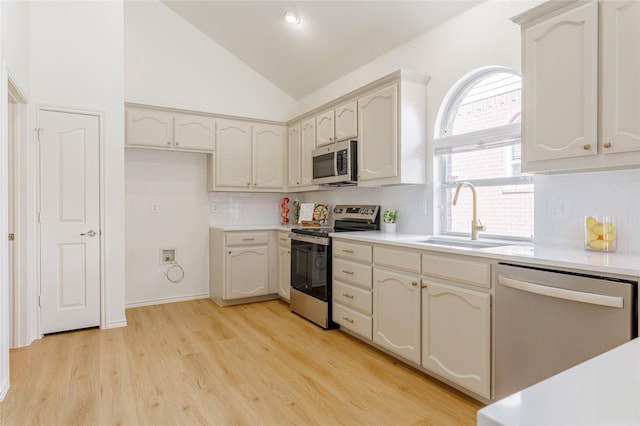 kitchen with tasteful backsplash, lofted ceiling, stainless steel appliances, light wood-type flooring, and a sink