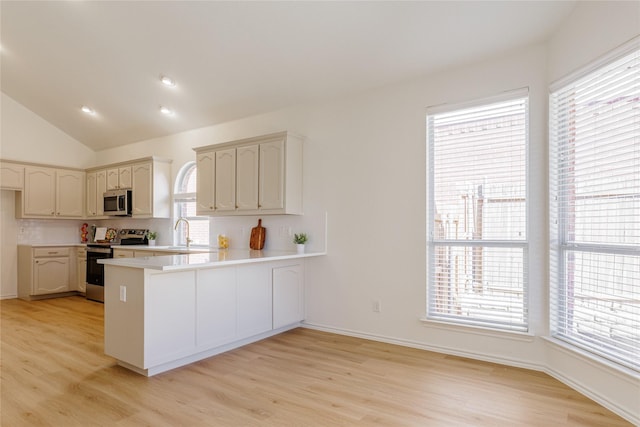 kitchen featuring light wood-style flooring, appliances with stainless steel finishes, a peninsula, vaulted ceiling, and light countertops