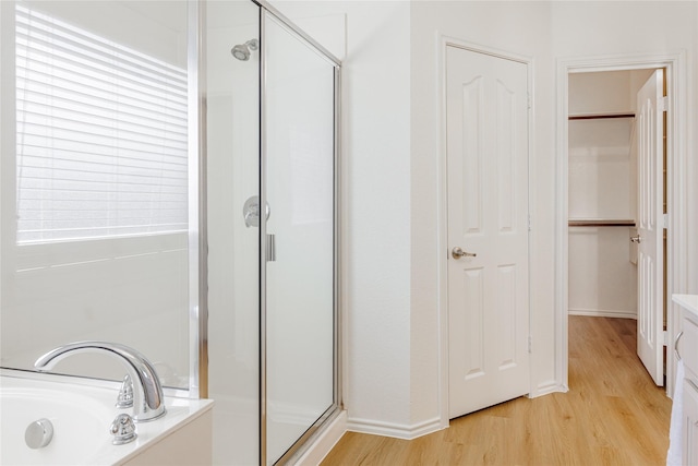 full bath featuring a bath, a stall shower, a closet, and wood finished floors