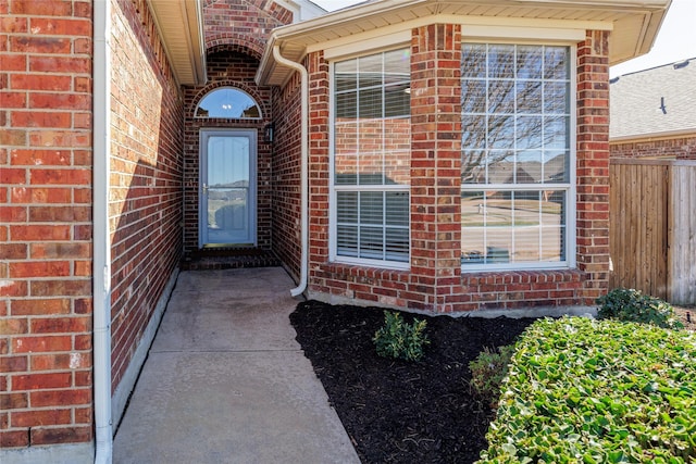 view of exterior entry with fence and brick siding