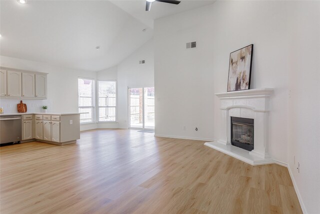 unfurnished living room featuring light wood-style floors, visible vents, a fireplace with raised hearth, and high vaulted ceiling