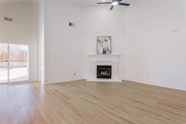 unfurnished living room featuring arched walkways, light wood-style flooring, a glass covered fireplace, ceiling fan, and baseboards