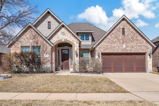 french country style house with a garage, a shingled roof, concrete driveway, a front lawn, and brick siding