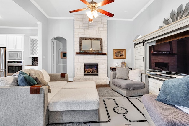 living area featuring arched walkways, ceiling fan, a fireplace, and crown molding