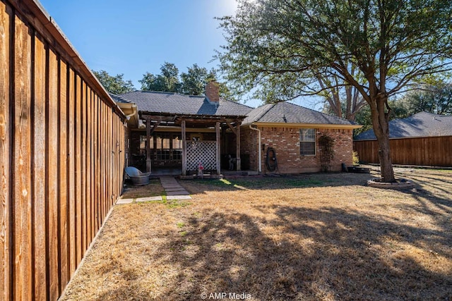 back of house featuring a shingled roof, a lawn, a chimney, fence, and brick siding