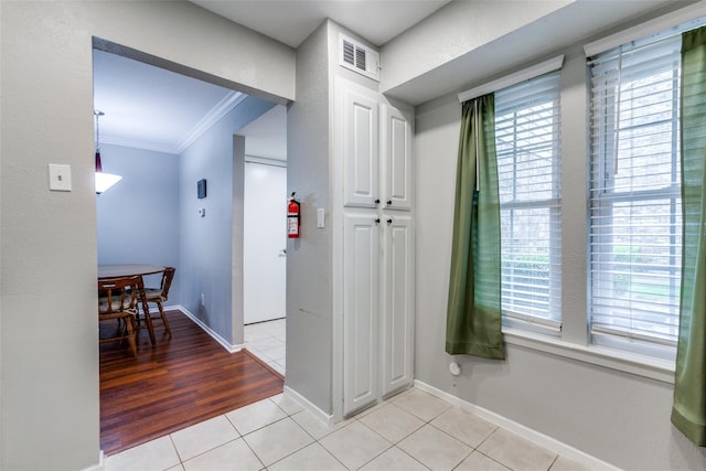 interior space with light tile patterned floors, a wealth of natural light, visible vents, and crown molding