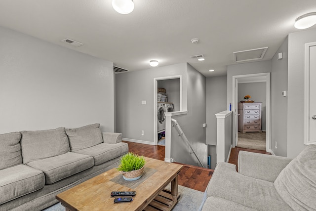 living room featuring washing machine and dryer, dark wood-type flooring, visible vents, baseboards, and attic access