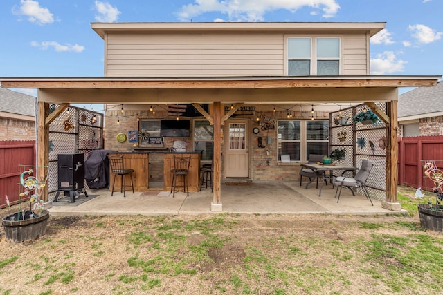 rear view of property with outdoor dry bar, a patio, brick siding, and a fenced backyard