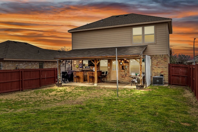 back of property at dusk with brick siding, a yard, central AC unit, a patio area, and a fenced backyard