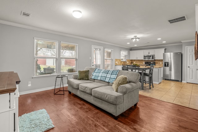 living room with ornamental molding, baseboards, visible vents, and light wood finished floors