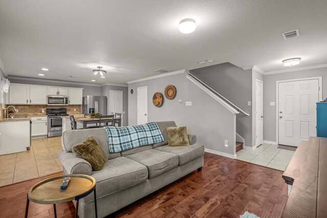 living room featuring light tile patterned floors, visible vents, baseboards, ornamental molding, and stairway