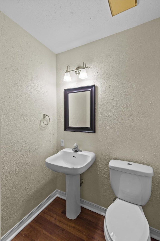 bathroom with baseboards, wood finished floors, and a textured wall