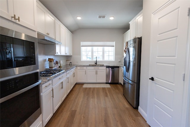 kitchen with light stone counters, under cabinet range hood, a sink, white cabinets, and appliances with stainless steel finishes