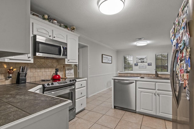 kitchen with light tile patterned floors, visible vents, white cabinets, ornamental molding, and stainless steel appliances